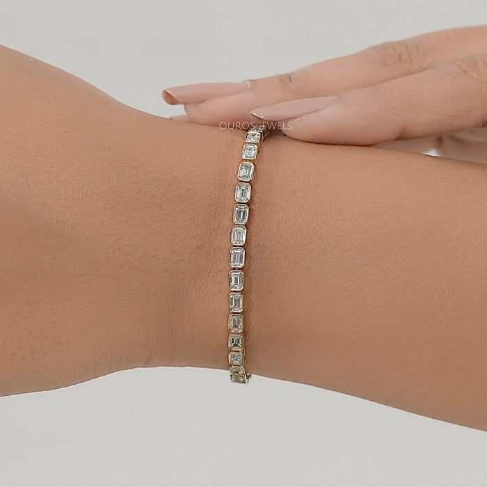 east west set emerald cut lab created diamonds bezel set tennis bracelet in yellow gold on hand
