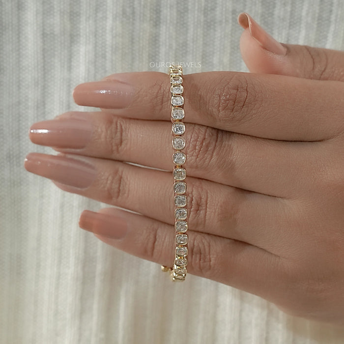 cushion cut ethically made diamonds bezel setting tennis bracelet in yellow gold on hand