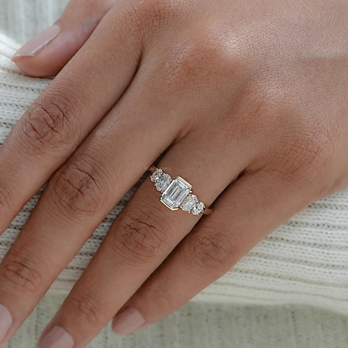emerald and oval cut diamond half bezel five stone engagement ring on model's finger
