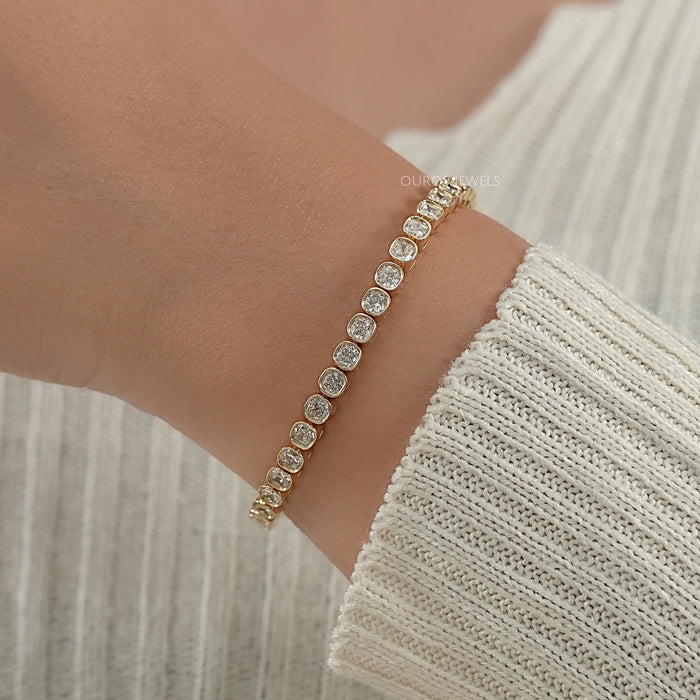 cushion cut lab produced diamonds bezel set tennis bracelet in yellow gold on hand