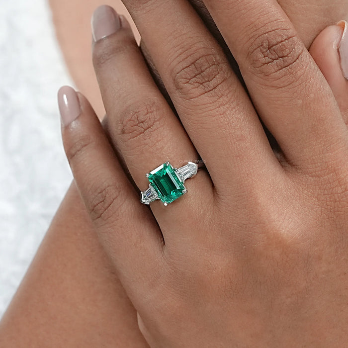 emerald gemstone and bullet-cut diamond three-stone engagement ring on model's finger