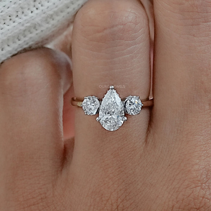 front view of three stone pear cut diamond hidden halo engagement ring in finger