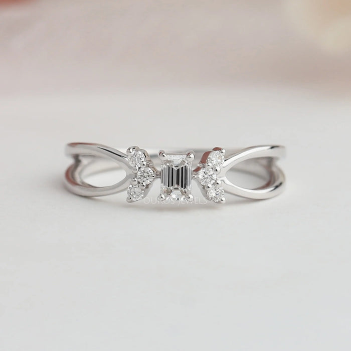 Close up view of man made emerald cut cluster diamond ring set in side small round cut diamonds.