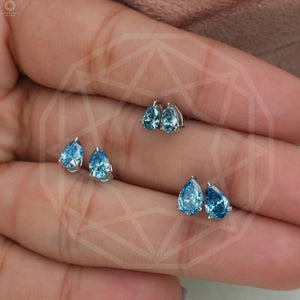 Three pairs of Blue Pear Shaped Diamond Stud Earrings, each with a pear shape, held in hand to show size and detail against a neutral background.